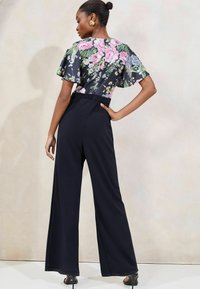 Bluza s cvjetnim uzorkom i kratkim lepršavim rukavima u kombinaciji s crnim hlačama širokog kroja visokog struka; glatka tkanina i suptilni sjaj.