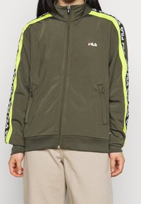 Oliwkowa kurtka zapinana na zamek z wysokim kołnierzem, z neonowo-żółtymi paskami po bokach i czarnymi akcentami z brandingiem. Dwie kieszenie na zamek z przodu.