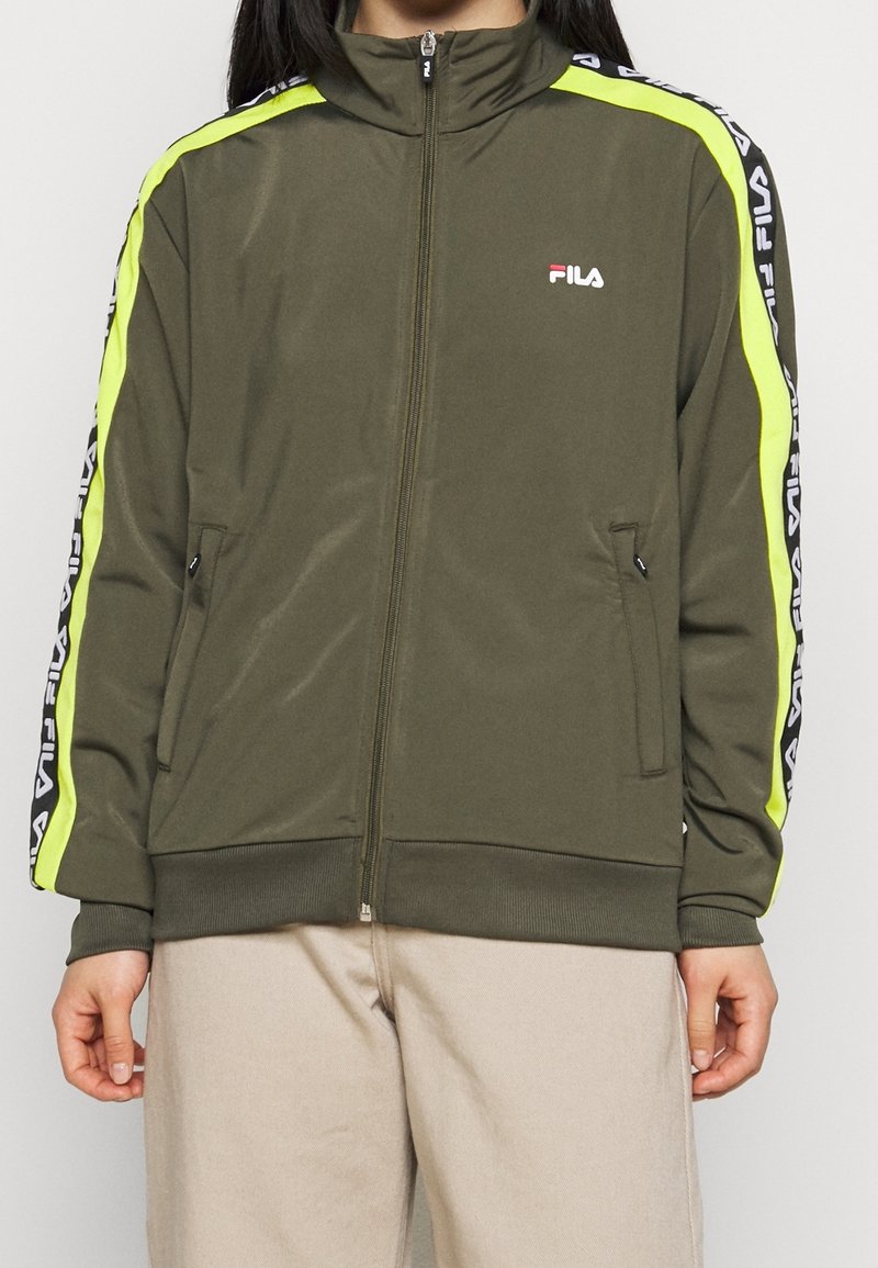 Oliwkowa kurtka zapinana na zamek z wysokim kołnierzem, z neonowo-żółtymi paskami po bokach i czarnymi akcentami z brandingiem. Dwie kieszenie na zamek z przodu.