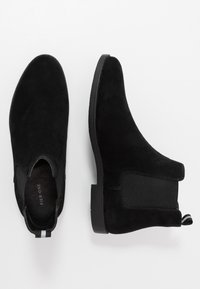 Stivaletti Chelsea in suede nero con pannelli laterali elasticizzati e un tab per il tiraggio. Suola piatta in gomma nera, punta rotonda, design minimalista.
