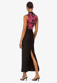 Schwarzes Maxikleid mit einem rosa blümchenbesetzten Oberteil, taillierter Silhouette, hohem Hals und Seitenschlitz; getragen mit schwarzen Riemchen-Heels.