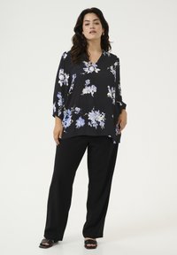 Zwarte bloes met lichte blauwe en witte bloemen, met een V-hals en driekwart mouwen, gecombineerd met zwarte wijde broek.