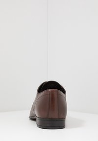 Hnědé kožené společenské boty s hladkým povrchem a jemnými švy, s nízkým podpatkem a zaoblenou špičkou. Zobrazeno ze zadní strany.