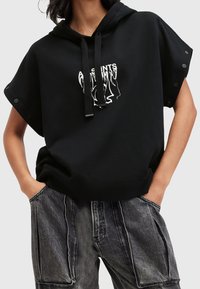 Černá zkrácená mikina s kapucí a šňůrkou, na přední straně s bílým grafickým designem. Krátké rukávy se zapínáním na patentky na ramenech.
