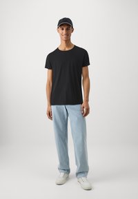 Black short-sleeve t-shirt paired with light blue loose-fitting jeans and white sneakers. The background is plain white.