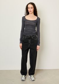Mörkgrå långärmad åtsittande topp med fyrkantig halsringning, kombinerad med lösa svarta jeans i denim och grå sneakers med gula accenter.