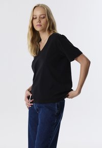 Zwarte korte mouwen V-hals top in een zachte, lichtgewicht stof; gecombineerd met blauwe denim jeans. Glad textuur, losse pasvorm en een eenvoudig ontwerp.