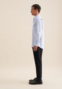 Lichtblauwe overhemd met lange mouwen, twee borstzakken, knoopmanchetten en een rechte snit, gecombineerd met zwarte broeken en donkere schoenen.