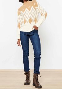 Pull en maille beige et blanc avec un motif en losanges, assorti à un jean skinny bleu foncé et des bottines à lacets marron.