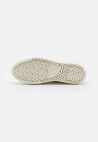 White rubber sneaker sole with a herringbone tread pattern, featuring a raised logo section. Smooth texture with a slight sheen.