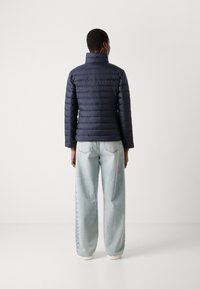 Giacca imbottita blu navy con colletto alto, design a righe orizzontali e maniche lunghe. Abbinata a jeans a gamba larga azzurri e sneakers bianche.