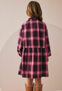 Abito a quadri viola e rosa con maniche lunghe, vita arricciata e colletto, abbinato a stivali color beige fino al ginocchio. Tessuto dalla consistenza liscia.