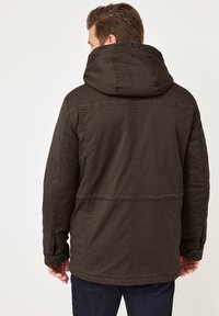 Dunkelbraune Kapuzenjacke mit strukturierter Stoff, sichtbaren Nähten und Knopfakzenten an den Manschetten. Ansicht von hinten.