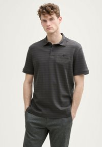 Czarna grafitowa koszulka polo z subtelnymi paskami, z trzema guzikami i kieszenią na lewej piersi, w zestawie z szarymi teksturowanymi spodniami.