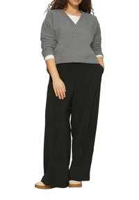 Grauer V-Ausschnitt-Pullover, der über einem weißen Hemd getragen wird, kombiniert mit weiten schwarzen Hosen. Das Outfit zeichnet sich durch eine lockere Passform und einen weichen Stoff aus.