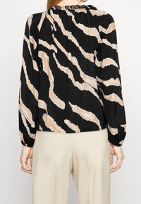 Blusa nera con motivo a strisce di tigre crema, scollatura arricciata e lunghe maniche a palloncino, realizzata in un tessuto leggero.