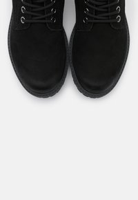 Bottines noires en suédine, dotées de lacets ronds et d'œillets en métal, avec une semelle en caoutchouc et un bout légèrement arrondi.