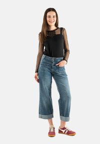 Camiseta negra de manga larga con mangas de tul con lunares, combinada con jeans de pierna ancha de color azul claro y zapatillas burgundy con detalles blancos.