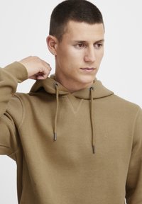 Light brown hoodie with a V-shaped neckline, drawstring hood, and embroidered logo. Soft texture and ribbed cuffs for comfort.