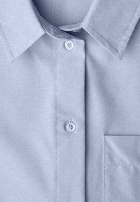 Chemise bleu clair en coton avec col, dotée d'une fermeture à boutons, d'une poche plaquée, et d'une texture lisse avec une finition soignée.