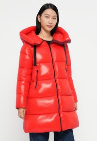 Rote Pufferjacke mit glänzender Oberfläche, großer Kapuze, schwarzem Zubehör, Reißverschlüssen und einem gesteppten Design zur Isolierung.