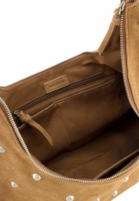 Interieur van een bruine suède handtas met een ritscompartiment, vlakke pocket en een lederen merklabel. Zachte textuur en een strak design.