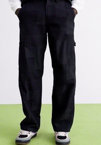 Black cargo pants made of cotton blend fabric, featuring a patchwork design, relaxed fit, side pockets, and a straight leg.