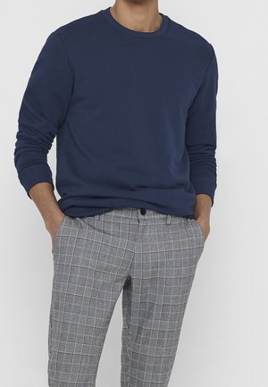 Sweat-shirt navy à manches longues, avec des bords côtelés et un col rond, associé à un pantalon à carreaux gris avec des rayures noires et blanches.