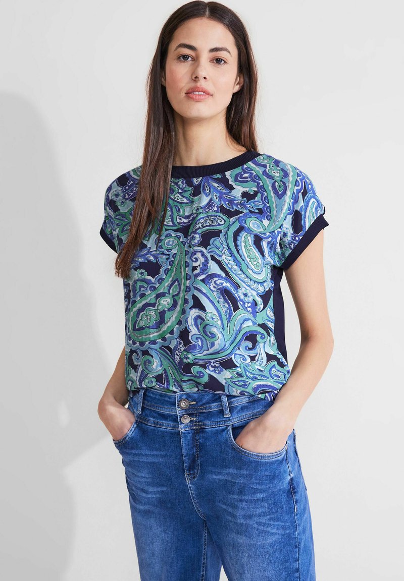 Top de manga corta en un patrón de paisley azul y verde sobre un fondo navy, con cuello redondo y paneles laterales oscuros en contraste.