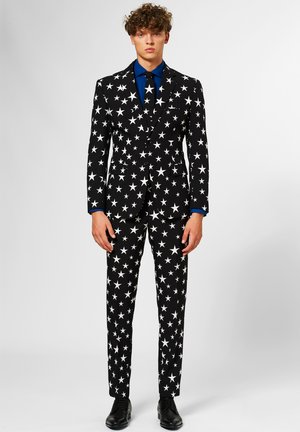 Black suit with white star pattern, double-breasted jacket, and slim-fit pants. Accented with a blue shirt underneath and black shoes.