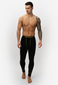 Black leggings with yellow stitching details and "CATERPILLAR" logo on the waistband. Made from a smooth fabric, fitted design.