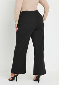 Svarta vida byxor med resårmidja och slät textur, med sidosömmar och avslappnad passform, kombinerade med svarta högklackade sandaler.