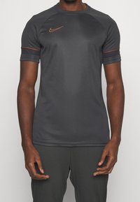 Harmaa lyhythihainen urheilupaita, joka on valmistettu kosteutta siirtävästä materiaalista, ja siinä on oranssi Nike-logo sekä korostukset hihoissa.