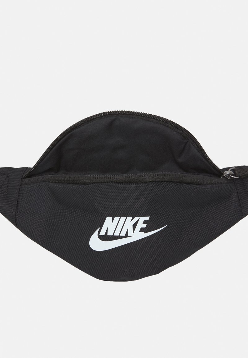 Bolsa de cintura negra de tela con cremallera, que presenta un destacado logo blanco de Nike en la parte frontal. Textura suave y forma curva.