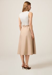 Beige midi-hame, jossa on sidottu vyötäröyksityiskohta, yhdistettynä muotoilultaan tiukkaan valkoiseen hihattomaan paita. Mallilla on päällään leopardikuosiset korot.