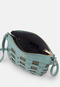 Ljusblå vävd handväska med dragkedjestängning, detaljer i guldton, och mörk inredning. Har en avtagbar rem och varumärkets detaljer.