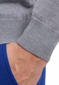 Grauer, gestrickter Pulloverbund mit geripptem Muster, kombiniert mit einem blauen Kleidungsstück. Der Bund sitzt eng und weist feine Nähdetails auf.