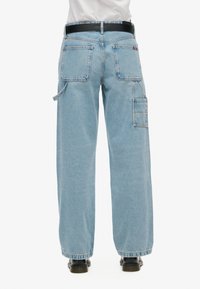 Pantalones cargo de mezclilla azul claro con un ajuste relajado, que cuentan con múltiples bolsillos, pierna recta y un cinturón negro. Se muestra vista trasera.