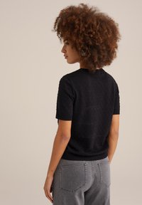 Melns īsām piedurknēm džemperis ar strukturētu rakstu un ribotām apkaklēm, apvienots ar pelēkiem džinsu biksēm, redzams no aizmugures.