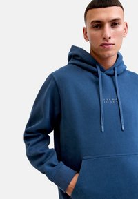 Sudadera azul marino con un bolsillo frontal, con capucha ajustable y estampado de logo sutil. Hecha de una tela suave y texturizada.