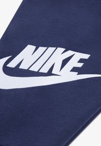 Țesătură din bumbac albastru marin cu un logo Nike alb proeminent și design swoosh. Textura pare netedă și țesută uniform.