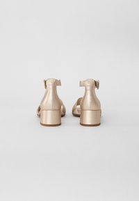 Beige metalliset korkokengät, joissa on nilkkaremmi ja solki, sisältävät lohko- ja avokärkimuotoilun. Litteä kumipohja.