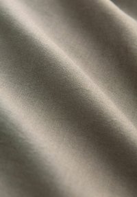 Khakifarbenes Gewebe, glatte Textur, mattes Finish und leicht geknitterte Oberfläche. Keine sichtbaren Muster oder Hardware-Details.