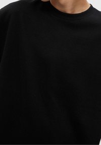 Svart crew neck t-shirt tillverkad av mjuk bomullsmaterial, med en slät struktur och avslappnad passform, utan synliga mönster eller detaljer.