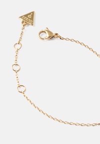 Pulseira de corrente de ouro com um encantador triangular com logotipo, fecho tipo lagosta e elos circulares para ajuste.