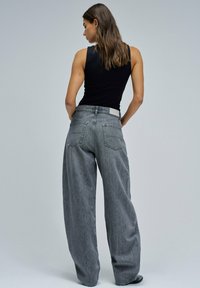 Jeans de pierna ancha grises con una textura desgastada, dos bolsillos traseros y una cinturilla lisa. Combinados con una camiseta sin mangas negra ajustada.