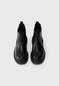 Μαύρες δερμάτινες μποτίνες ankle με ελαστικές πλαϊνές επιφάνειες, στρογγυλές μύτες και χοντρές καουτσούκ σόλες. Δύο λαβές για εύκολη τοποθέτηση. Λείο στυλ.