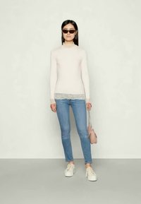 Top de mangas largas en rosa claro con encaje, combinado con jeans ajustados azules y zapatillas blancas. Los accesorios incluyen un pequeño bolso rosa y gafas de sol.