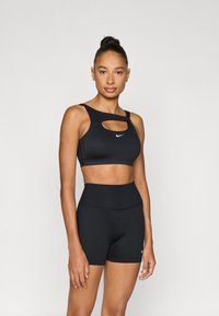 Fekete sportmelltartó kivágott mint ával, fehér logóval, hozzáillő magas derekú fekete rövidnadrággal. Simább, rugalmas anyag.