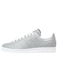 Zapatillas plateadas con un patrón texturizado de escamas de pez, cordones blancos y suela de goma blanca. Marca en el lateral. Diseño clásico de corte bajo.